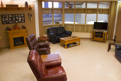 The Long Term Care Unit day room including seating, tables, pictures, windows, and a TV.